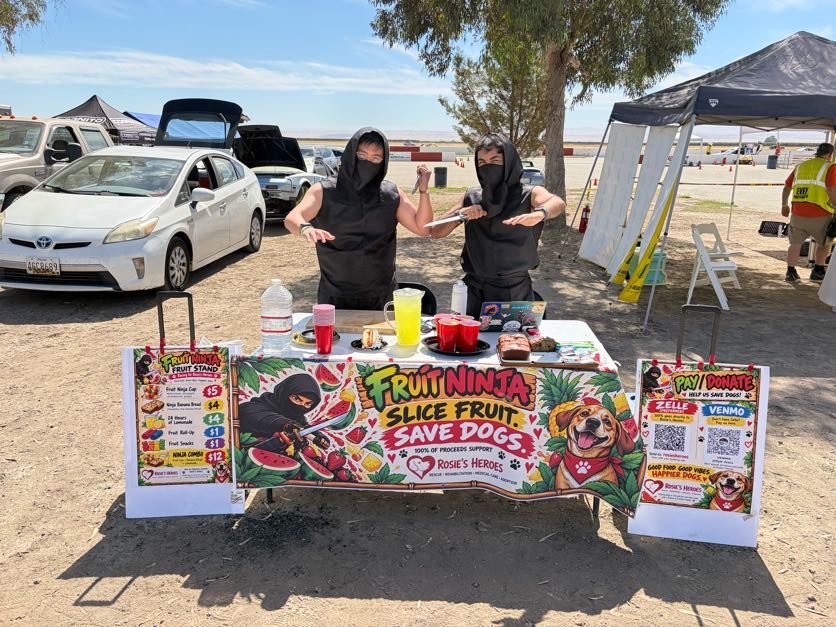 Two RN Racing members in ninja outfits behind the Fruit Ninja fruit stand supporting Rosies Heroes.