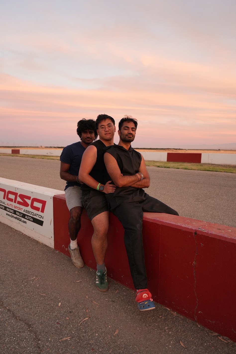 Three RN Racing members pose together beside the track at sunset.